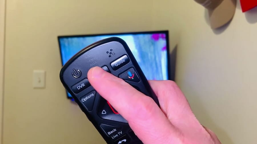 Hand holding a Dish Network remote control pointing toward a TV