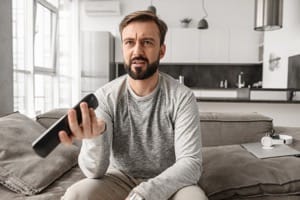 frustrated person on couch holding TV remote watching buffering screen