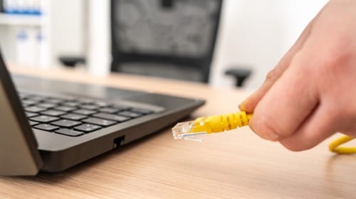 Close-up of hand holding Ethernet cable ready to connect to a laptop for stable Zoom calls